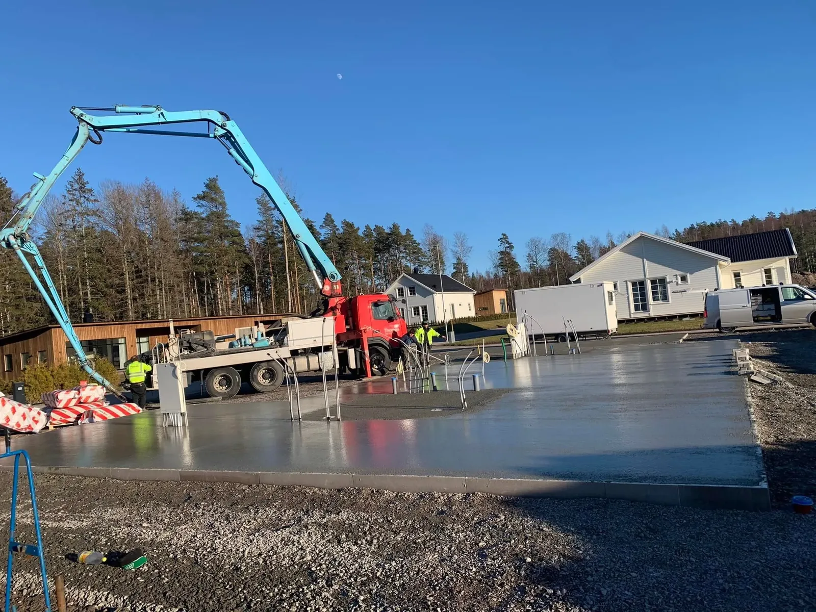 Betongpump gjuter en husgrund på en villatomt medan arbetare jämnar till betongen