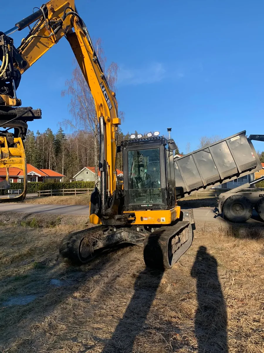 Gul grävmaskin i arbete bredvid en tippvagn